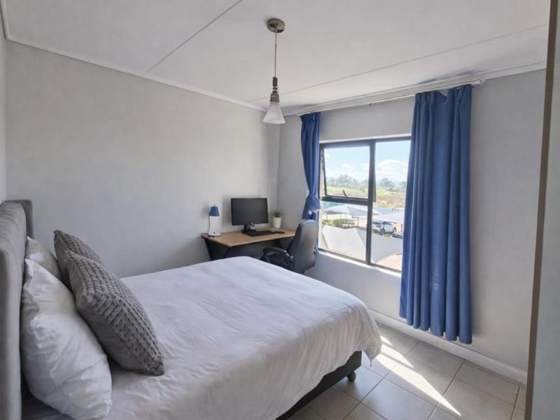 A bright bedroom featuring tiled flooring, a pendant light, and an aluminium window frame with views of the surrounding area.