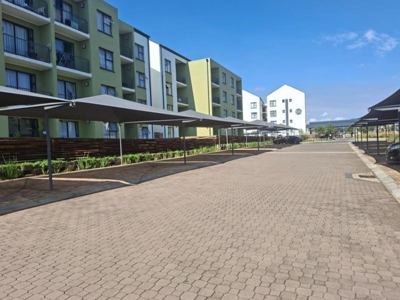 Exterior view of an apartment complex featuring paved parking areas with shade cloth carports and multi-story residential buildings.