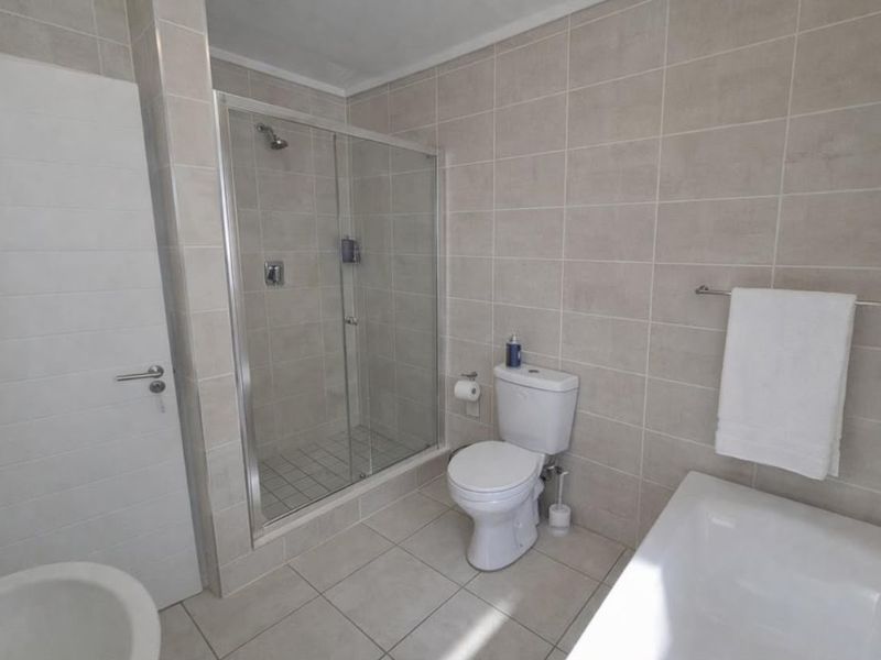 A clean, modern bathroom featuring a glass-enclosed shower, a separate bathtub, a toilet, and neutral-toned wall and floor tiling.