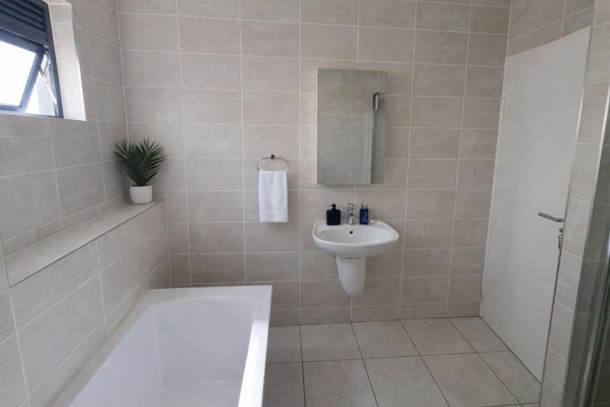 A clean, modern bathroom featuring neutral wall and floor tiles, a wall-mounted basin, and a built-in bathtub.