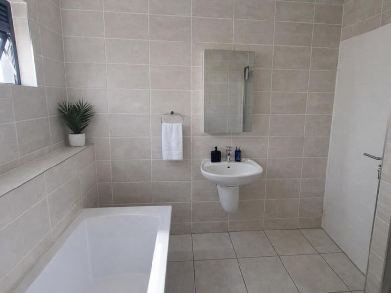 A clean, modern bathroom featuring neutral wall and floor tiles, a wall-mounted basin, and a built-in bathtub.