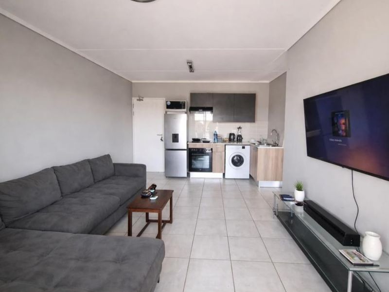 Open-plan living area featuring a compact kitchen with built-in cabinetry, oven, hob, and tiled flooring throughout.