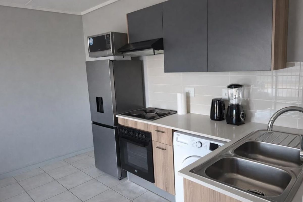 Modern kitchen featuring dark grey upper cabinets, wood-finish lower cabinetry, stainless steel sink, built-in oven, electric hob, and tiled flooring.