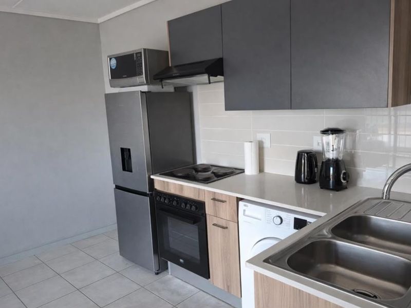 Modern kitchen featuring dark grey upper cabinets, wood-finish lower cabinetry, stainless steel sink, built-in oven, electric hob, and tiled flooring.