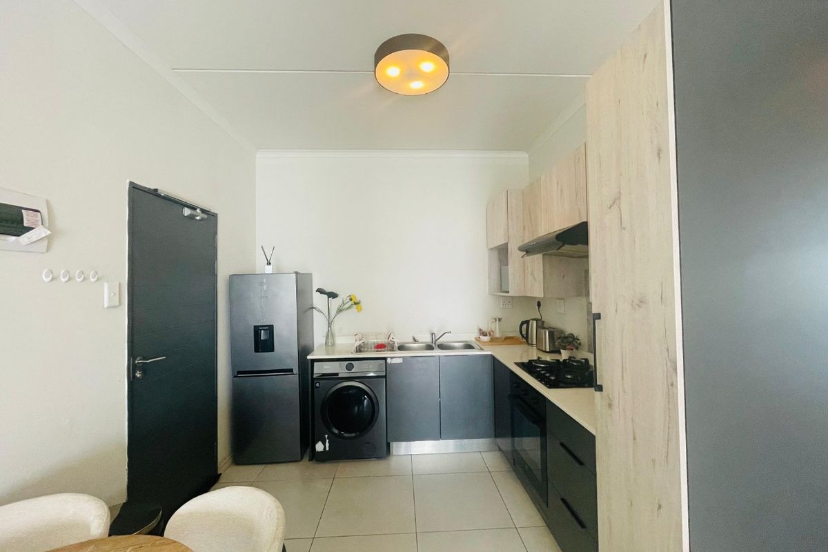 Modern kitchen featuring two-tone cabinetry, built-in oven, gas hob, extractor fan, and tiled flooring, with integrated space for laundry appliances.