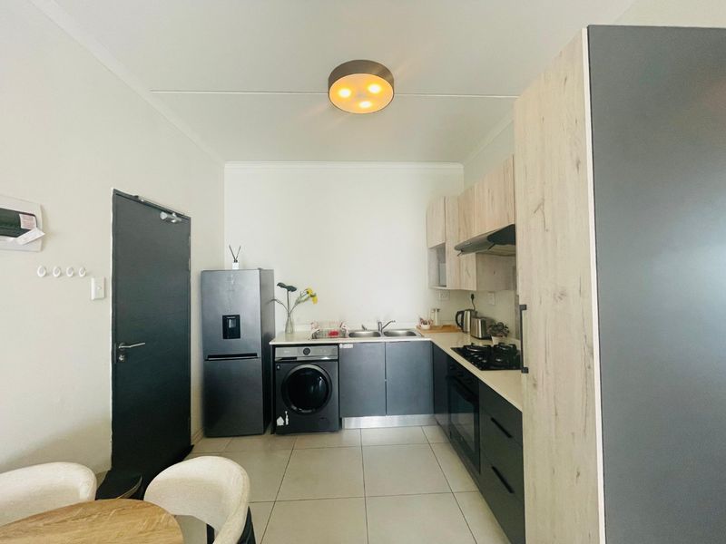 Modern kitchen featuring two-tone cabinetry, built-in oven, gas hob, extractor fan, and tiled flooring, with integrated space for laundry appliances.