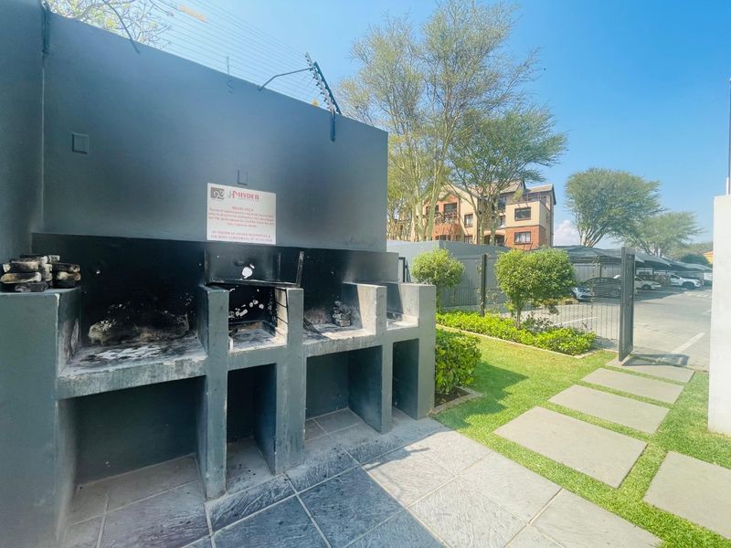 Outdoor communal braai area featuring built-in masonry barbecue stations, set within a landscaped garden with paved pathways and secure perimeter fencing.