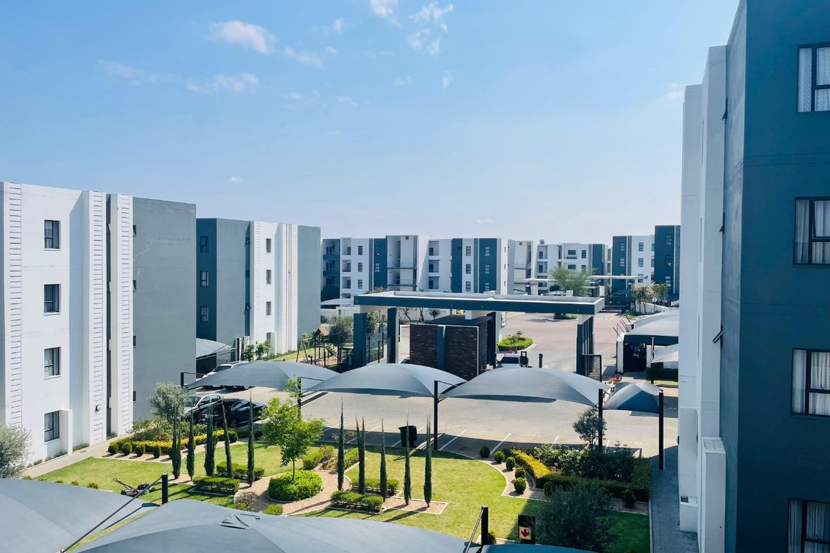 An elevated view of a modern apartment complex featuring landscaped gardens, secure gated access, and covered parking bays.