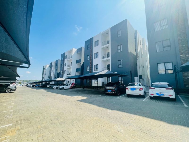 Exterior view of a modern multi-story apartment complex featuring paved parking bays with shade cloth carports.