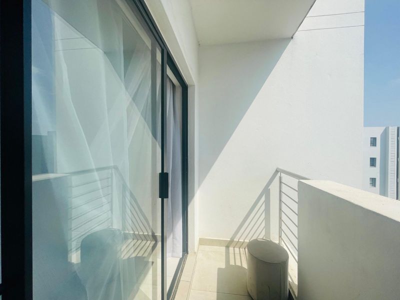 A clean, modern balcony featuring tiled flooring, a metal balustrade, and large sliding glass doors providing access to the interior living space.