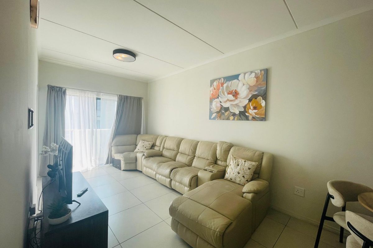 A bright living room featuring neutral tiled flooring and a sliding glass door providing access to an outdoor area.