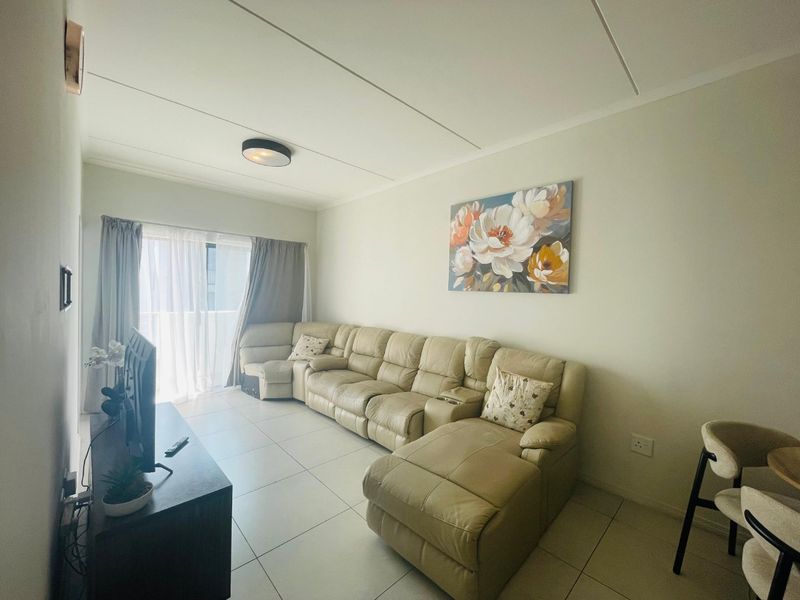 A bright living room featuring neutral tiled flooring and a sliding glass door providing access to an outdoor area.