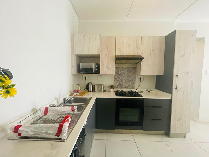 Modern kitchen featuring two-tone cabinetry, stone countertops, built-in gas hob, electric oven, extractor fan, and a double basin sink with tiled flooring.