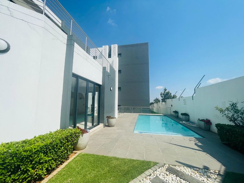 A well-maintained outdoor pool area featuring a tiled patio, glass balustrade, and direct access to the apartment via sliding glass doors.