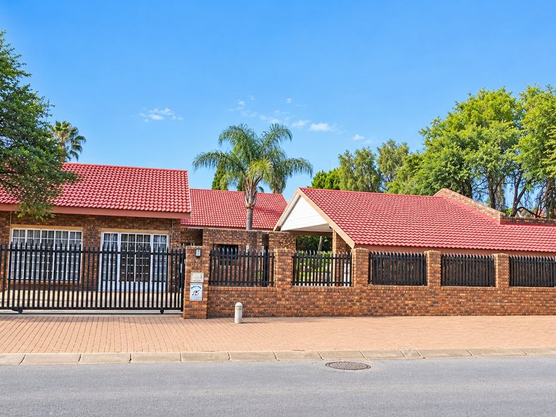Front view of a brick house featuring a tiled roof, secure perimeter fencing, and a paved driveway with an integrated carport.