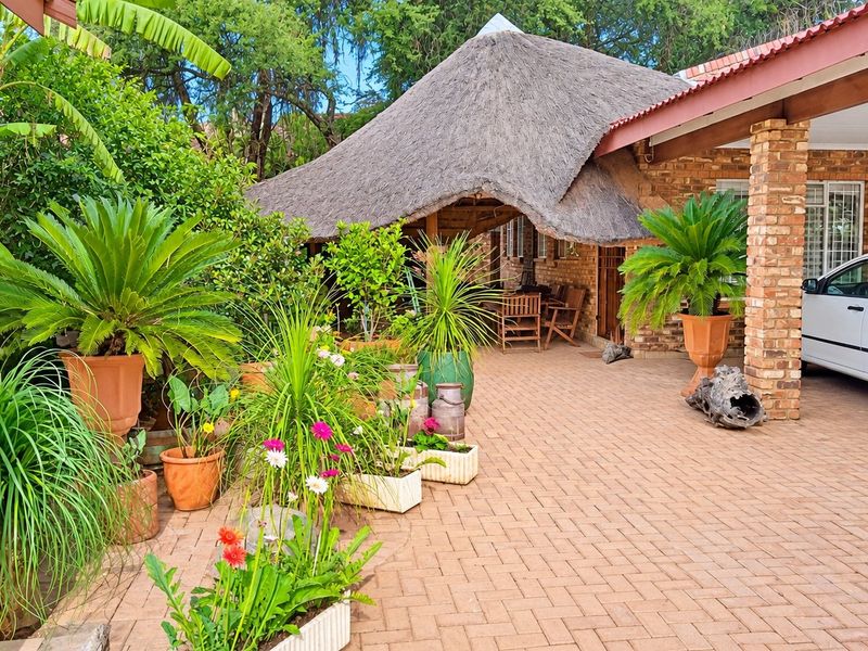 A covered outdoor patio area featuring a traditional thatched roof, exposed brick pillars, and paved flooring, providing a charming space for outdoor relaxation.