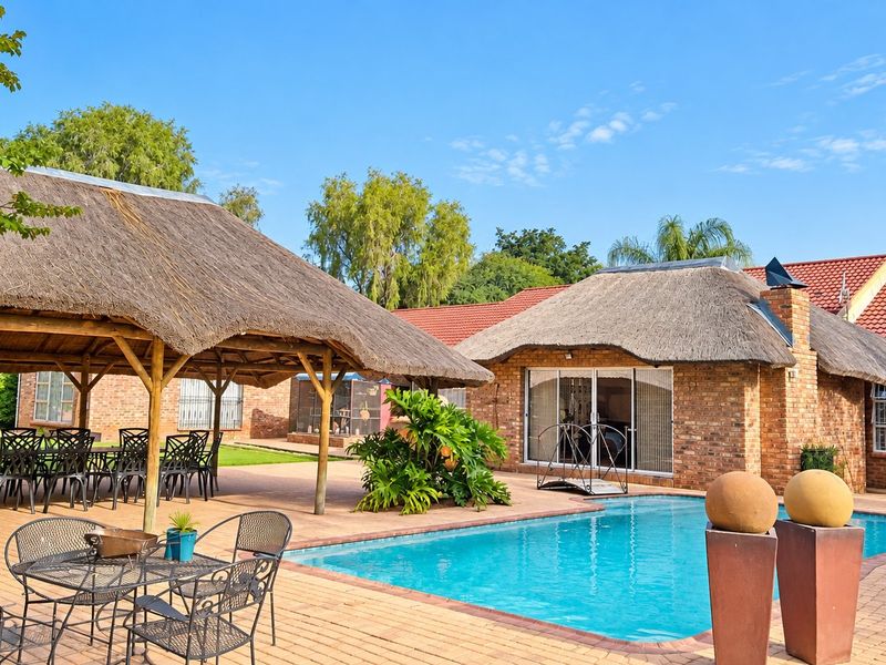Outdoor entertainment area featuring a swimming pool, brick-paved patio, and a traditional thatched lapa, perfect for relaxed outdoor living.