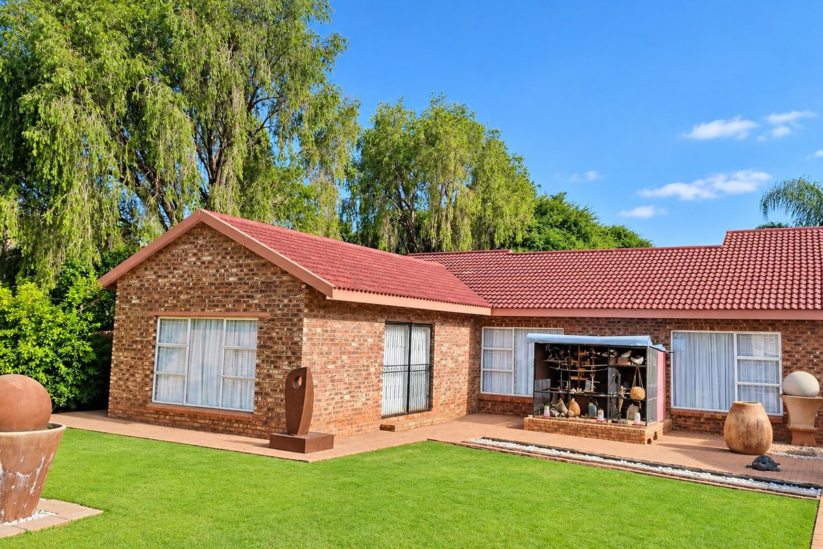 A well-maintained rear exterior view of a face brick house featuring a tiled roof, paved patio area, and landscaped garden.
