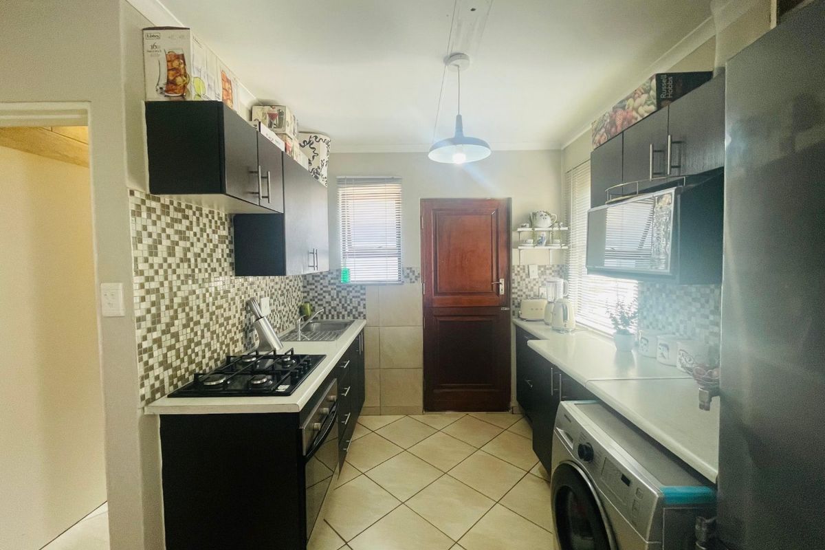 A functional galley-style kitchen featuring dark cabinetry, mosaic tile backsplashes, gas hob, built-in oven, and tiled flooring with direct access to an exterior door.