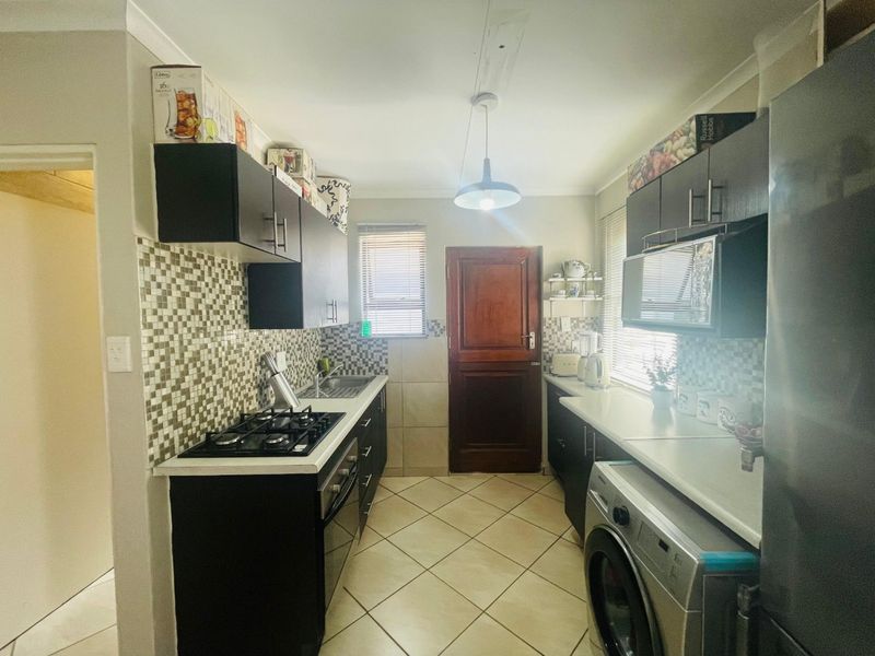 A functional galley-style kitchen featuring dark cabinetry, mosaic tile backsplashes, gas hob, built-in oven, and tiled flooring with direct access to an exterior door.