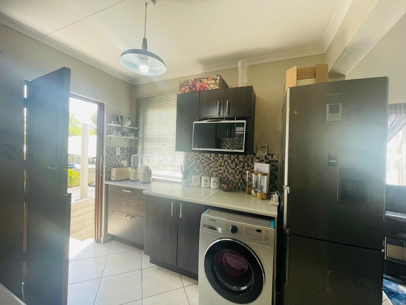 Compact kitchen featuring dark cabinetry, mosaic tile backsplash, laminate countertops, and integrated appliance space with direct access to the exterior.