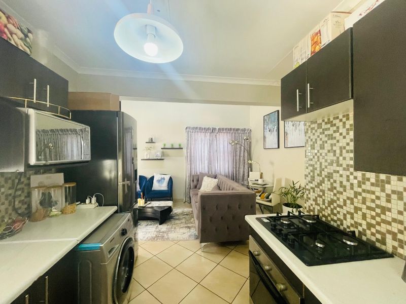 Open-plan kitchen and living area featuring dark cabinetry, a gas hob, mosaic backsplash, and tiled flooring, creating a functional and connected living space.