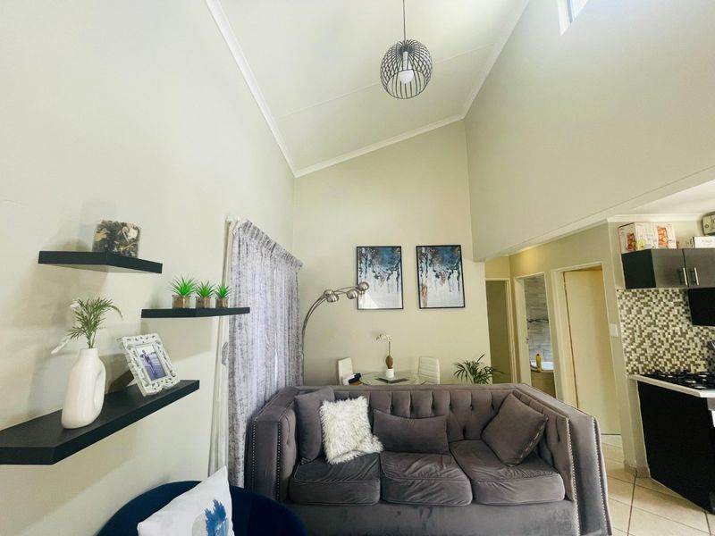 Open-plan living area featuring a high vaulted ceiling, tiled flooring, and an adjoining kitchen with mosaic backsplash and built-in cabinetry.