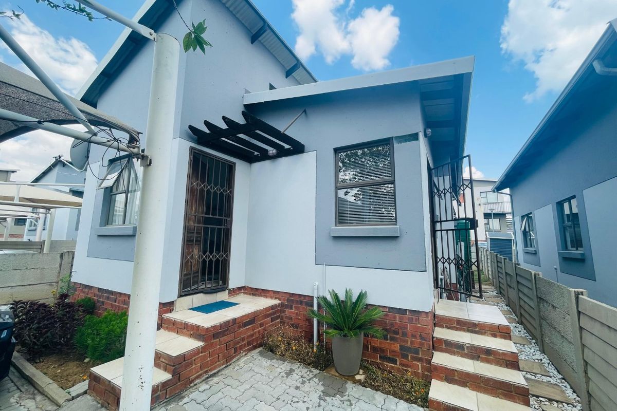 Rear exterior view of the house featuring a paved patio area, tiled steps, and secure metal gates.