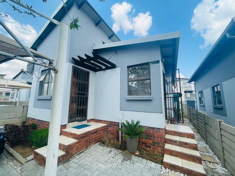 Rear exterior view of the house featuring a paved patio area, tiled steps, and secure metal gates.