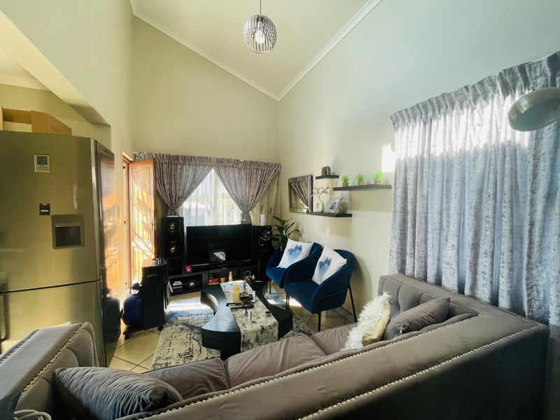 A bright living room featuring a high vaulted ceiling, tiled flooring, and large windows with curtains, creating an airy and open atmosphere.