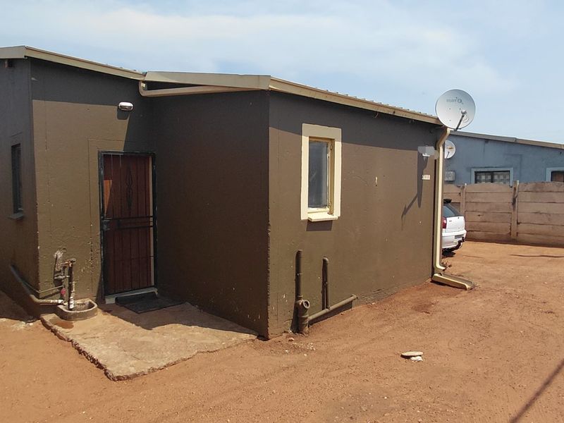 Rear view of the property showing the exterior wall, security door, and surrounding yard area with boundary walling.
