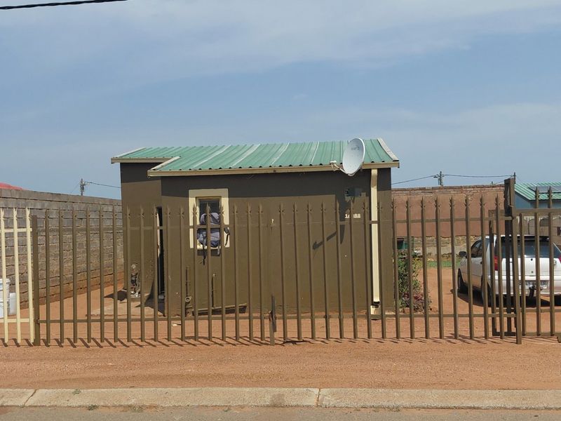 Front view of a detached residential property featuring a metal roof, perimeter fencing, and a gated driveway area.