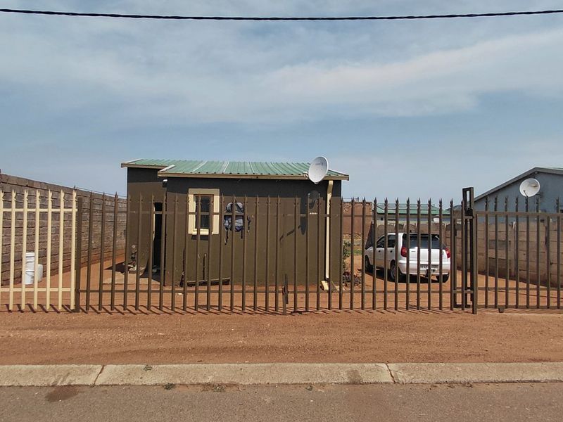Front view of a residential property featuring metal palisade fencing, a gated entrance, and a structure with a corrugated metal roof.