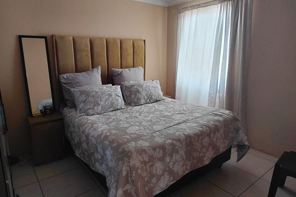 A functional bedroom featuring tiled flooring and natural light through window curtains, providing a comfortable and neutral living space.