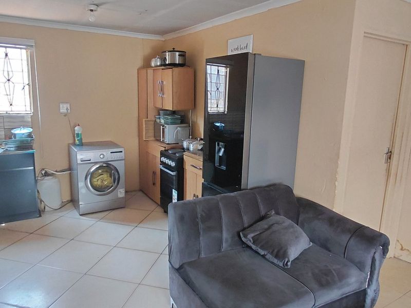 Open plan living area featuring a compact kitchen corner with tiled flooring, built-in cabinetry, and a sink, showing signs of wall moisture damage.