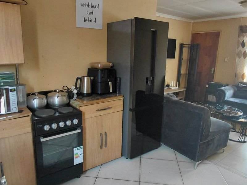 Open-plan kitchen and living area featuring tiled flooring, wooden cabinetry, and a freestanding stove, offering a functional layout for daily living.