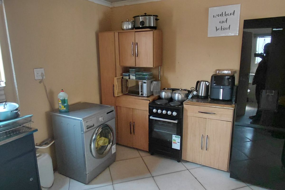 Compact kitchen featuring tiled flooring, built-in cabinetry, a stainless steel sink, and a freestanding stove with security bars on the window.