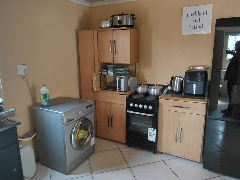 Compact kitchen featuring tiled flooring, built-in cabinetry, a stainless steel sink, and a freestanding stove with security bars on the window.