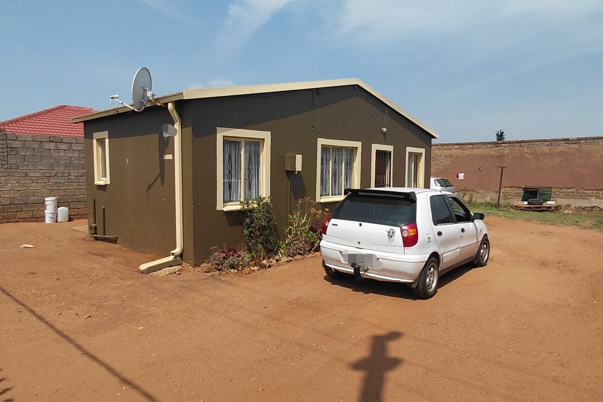 Rear view of a detached house featuring a large unpaved yard, perimeter walling, and exterior guttering systems.