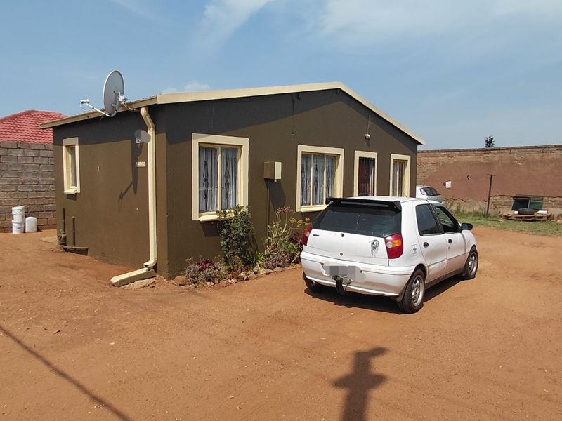Rear view of a detached house featuring a large unpaved yard, perimeter walling, and exterior guttering systems.