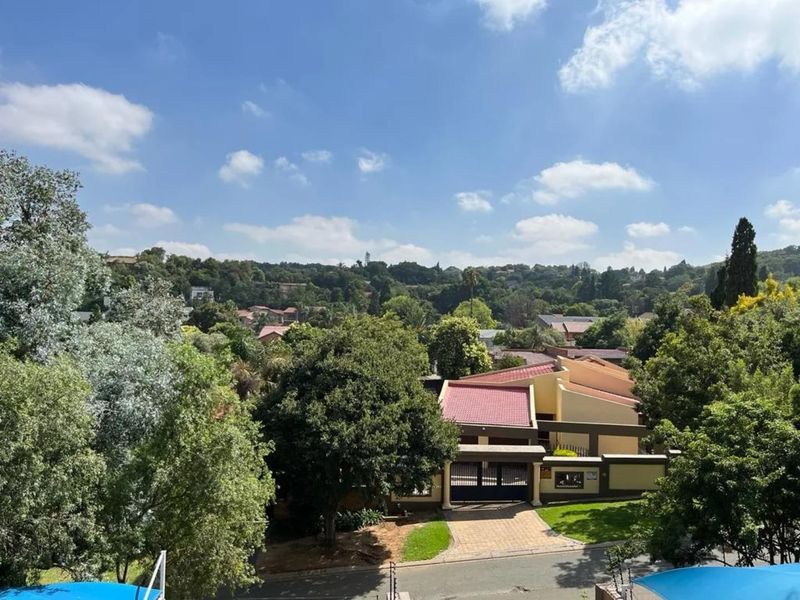 Elevated view overlooking a residential neighbourhood with mature trees, paved driveway, and a secure gated entrance.