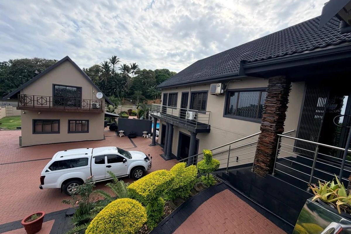 A well-maintained rear exterior view featuring a paved courtyard, stone-clad architectural detailing, and a balcony overlooking the property grounds.