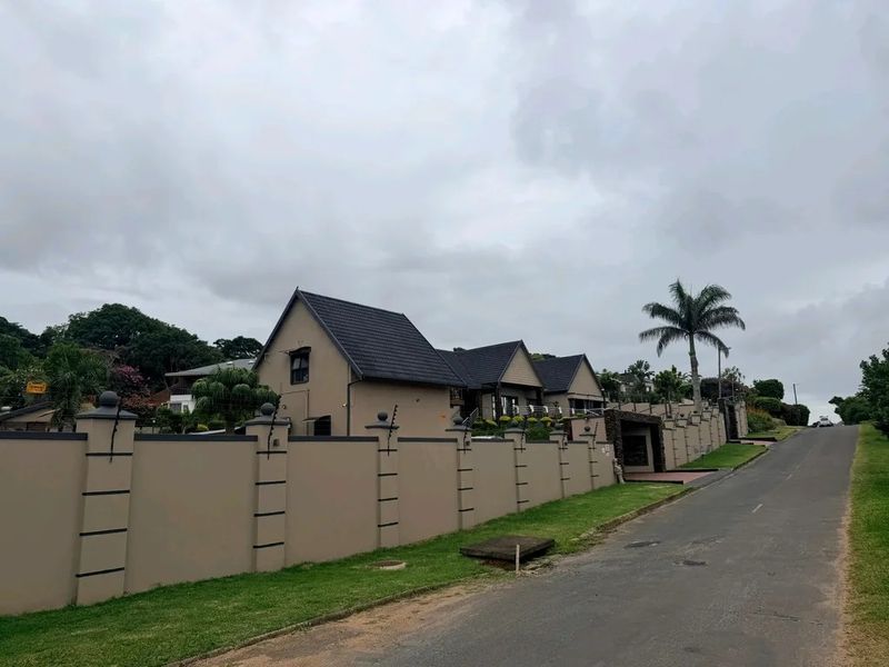Street view of the property featuring a secure perimeter wall with electric fencing and a well-maintained tiled roof structure.