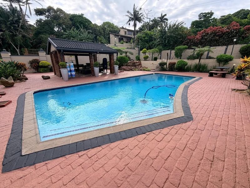 Outdoor pool area featuring a swimming pool, paved surround, and a covered patio structure set within a landscaped garden.