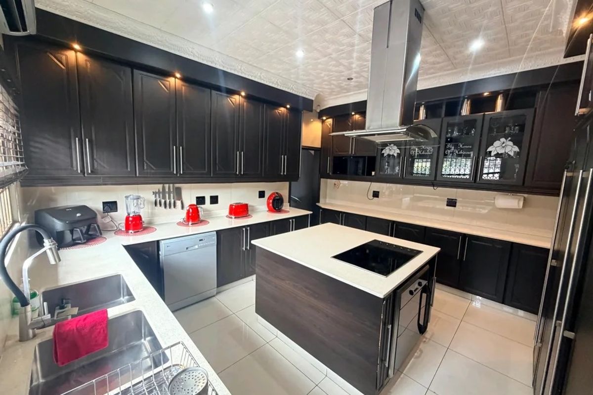 Modern kitchen featuring dark cabinetry, a central island with a built-in cooktop, stainless steel extractor fan, and light-colored countertops.