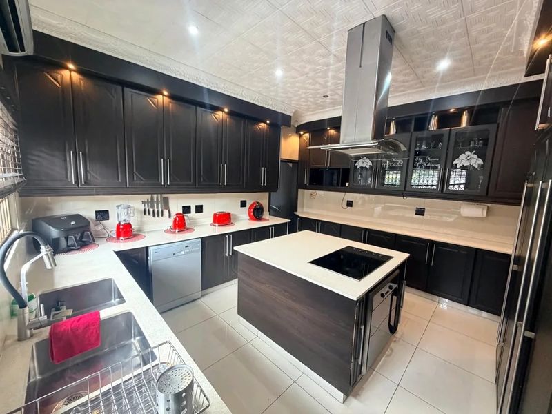 Modern kitchen featuring dark cabinetry, a central island with a built-in cooktop, stainless steel extractor fan, and light-colored countertops.