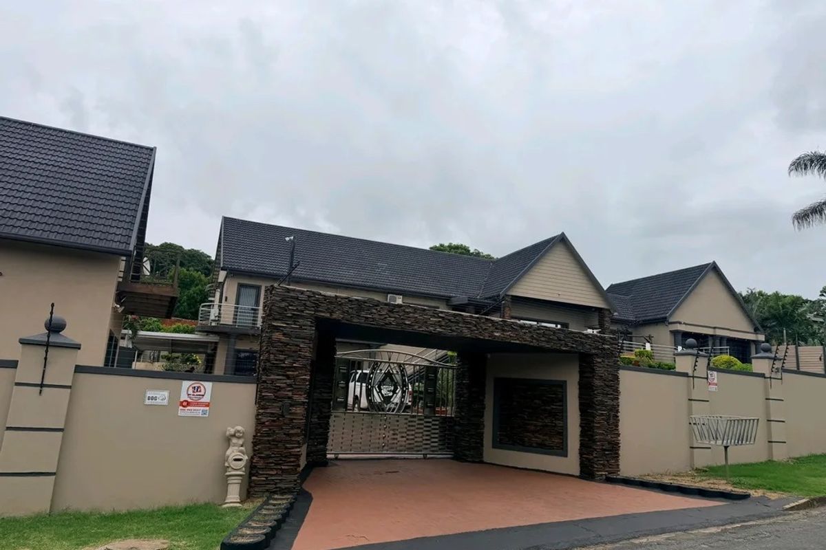 Front elevation of a modern residence featuring a prominent stone-clad entrance gate, secure perimeter walling, and a well-maintained paved driveway.