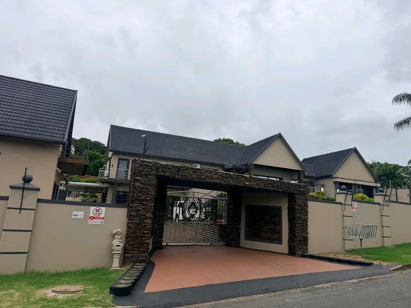 Front elevation of a modern residence featuring a prominent stone-clad entrance gate, secure perimeter walling, and a well-maintained paved driveway.