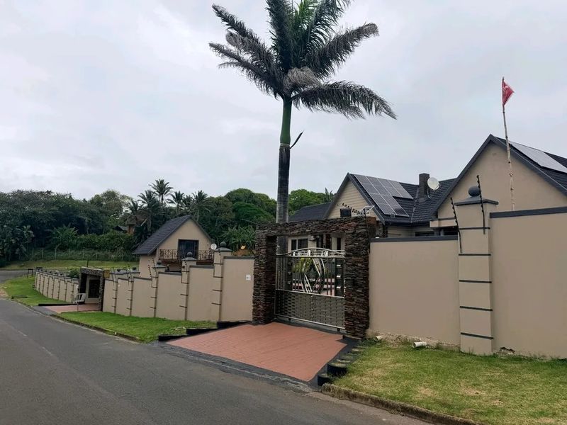 Front exterior view of the property featuring a secure perimeter wall, metal driveway gate with stone cladding, and solar panels installed on the roof.