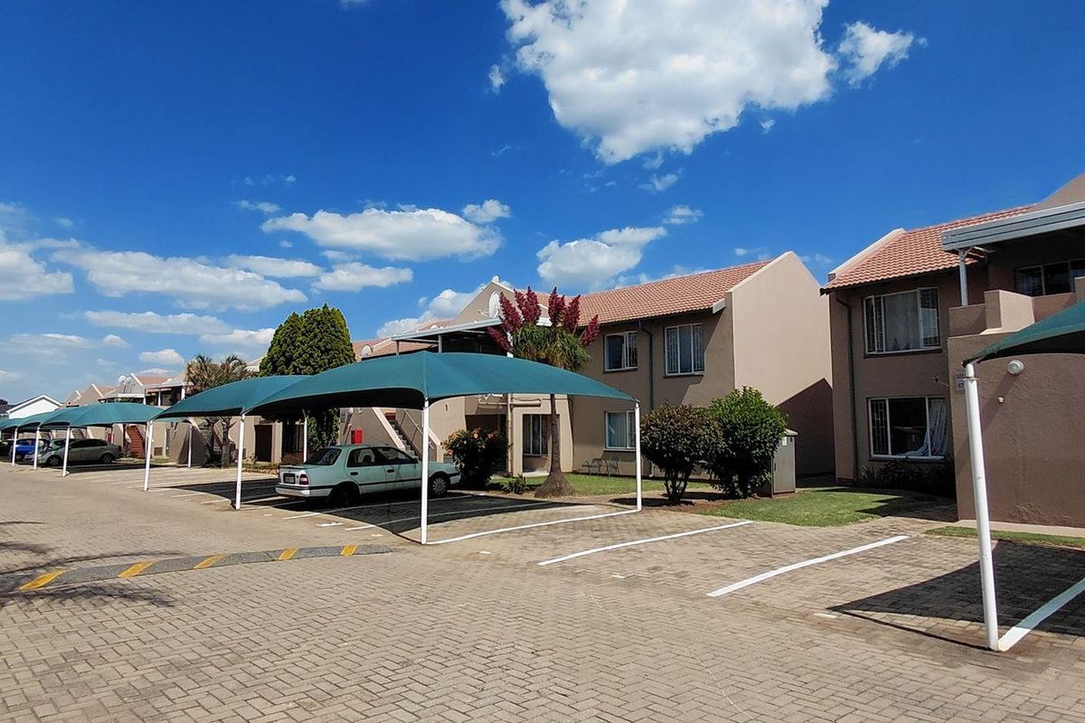 Exterior view of an apartment complex featuring paved parking areas with shade cloth carports and well-maintained building facades.